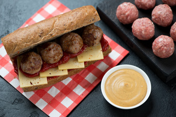 Submarine sandwich with fried meatballs and cheese, studio shot over black stone surface