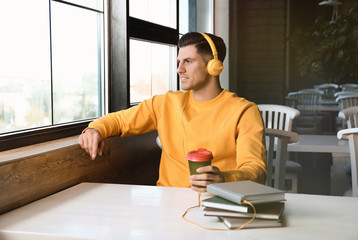 Man with headphones connected to book at table in cafe