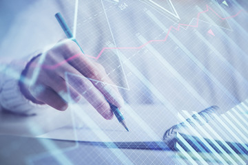 Financial forex graph displayed on hands taking notes background. Concept of research. Double exposure