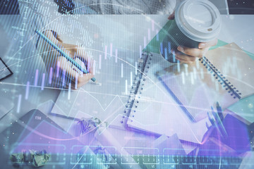 Financial forex graph displayed on hands taking notes background. Concept of research. Multi exposure