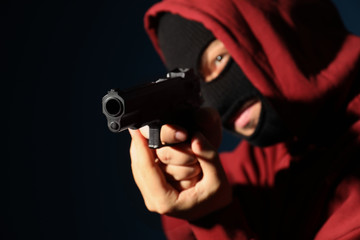 Man in mask holding gun on dark background, focus on hands