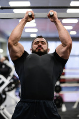 Fototapeta na wymiar powerful active strong caucasian man with beard making chin ups on crossbar in athletic sport gym