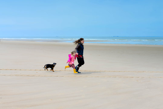 cute little girl playing on the beach with her mom and baby dog