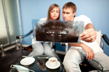 Young couple man and woman sitting in dental clinic, looking at dental picture and drinking tea. Dental health and medical care concept