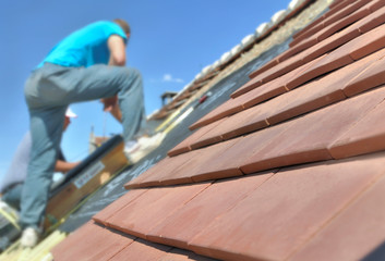 new red tiles on a roof and worker standing background against the blue sky