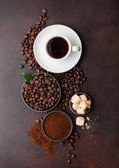 White cup of fresh raw organic coffee with beans and ground powder with cane sugar cubes with coffee tree leaf on brown background. Top view