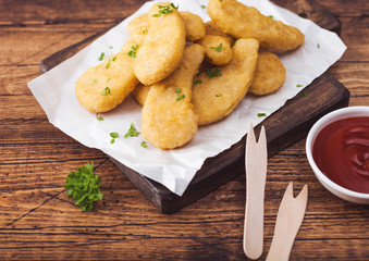 Buttered chicken nuggets on chopping board with wooden forks and ketchup on wooden background.