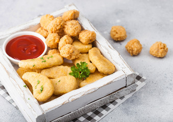 Buttered chicken nuggets and popcorn bites in white vintage wooden box with ketchup on light background.