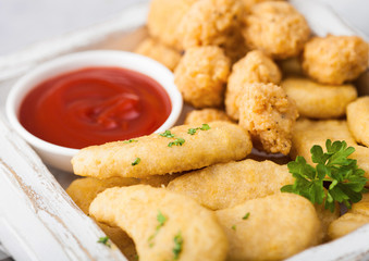 Buttered chicken nuggets and popcorn bites in white vintage wooden box with ketchup on light background. Macro