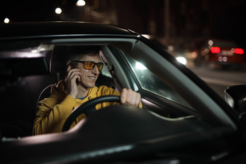 Driver man distracted to talks by mobile phone while driving car at night time, danger habit