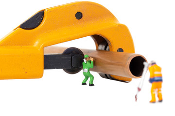 Naklejka premium Miniature scale model construction workers with a copper pipe and a pipe cutter isolated. Plumbing industry concept