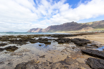 Coastline and sand beach Playa de Famara with mountain range and ocean waves in the north west of canary island Lanzarote