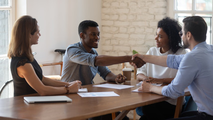 Happy diverse business partners shaking hands after successful negotiation