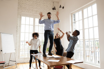 Excited leader dancing with diverse business team in boardroom