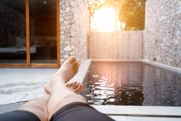 Man feet on sun bathing bed resting relaxing beside private swimming pool. leisure vacation lifestyle. Summer concept about people lying on deck chair in vacation.