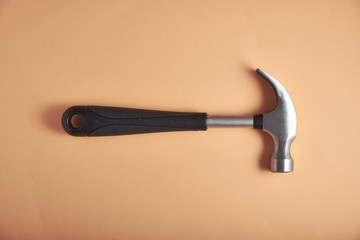 Metal hammer with a plastic handle on a light orange background, top view