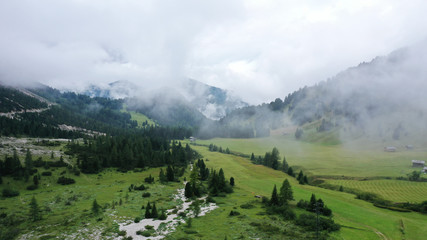 Fototapeta na wymiar Aerial view of pine spruce forest on green meadow with low clouds and fog. Mountain range, Dolomites, South Tyrol, Italy.