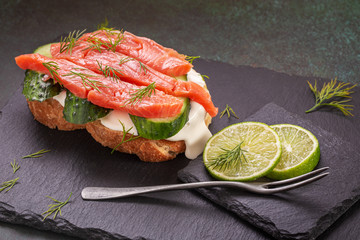 Salted salmon sandwich with cream cheese and cuccumber on slate platter closeup