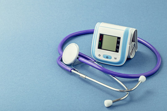 Stethoscope and wrist blood pressure monitor on blue background with copy space