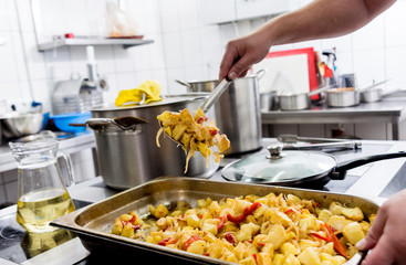Chef cooks fried potatoes with pieces of meat in a restaurant kitchen