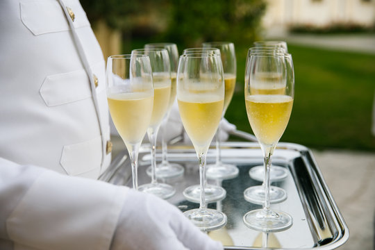A waiter in a white tuxedo holds a tray with glasses of sparkling wine so that each guest can refresh themselves with a SIP of champagne or Prosecco at a wedding party on a hot summer day in Italy