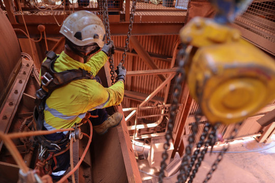 Rope access rigger wearing harness safety helmet heavy duty glove abseiling working in fall arrest position commencing using a lifting chain block hoist lifting a heavy load at construction site WA 