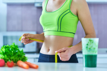Diet woman in sportswear with measuring tape and a green smoothie for losing weight. Vegetables...