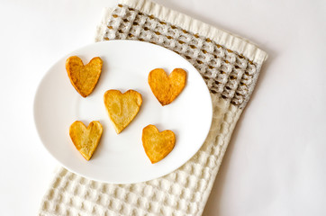 Fried French fries hearts on a white oval plate. A gift for a loved one. Close up. Selective focus