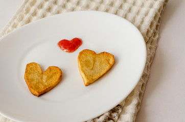 Two fried potato hearts and a red sauce heart on an oval white plate. Surprise for a loved one for the holiday. Top view. Close up.