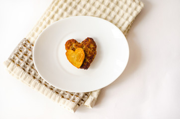 Fried cutlet in the shape of a heart, on it lies a heart of fried potatoes on a white oval plate. A gift for a loved one. Close up. Selective focus