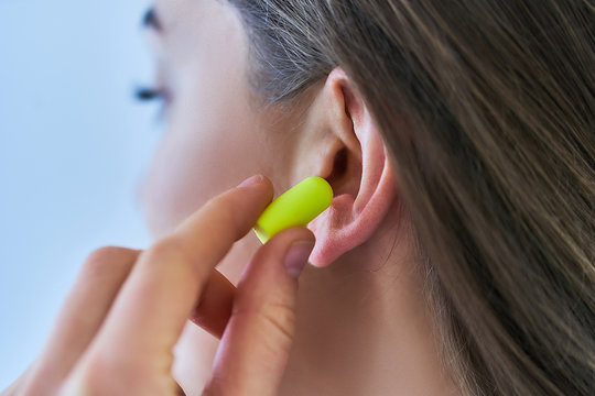 Young brunette woman putting earplugs into her ears for loud noise protection