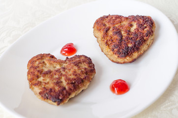 Two heart-shaped fried cutlets on an oval white plate lie on the table on a cream-colored kitchen napkin. Surprise for a loved one for the holiday. Top view. Close up.