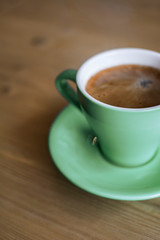 Freshly made coffee in a green ceramic cup on a wooden table.