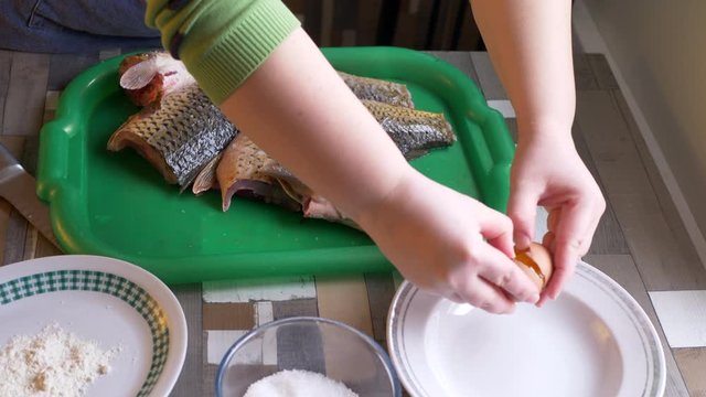 Hands of young woman with knife clean scales of fresh fish on kitchen table. Girl prepares fish for frying