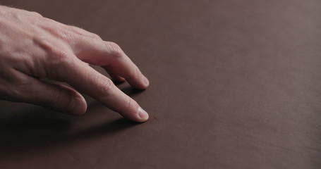 man hand shows scar on brown leather piece closeup
