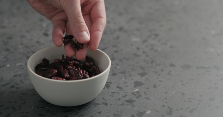 man hand take dried cranberry from white bowl on terrazzo countertop