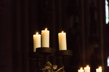 Drei brennende Kerzen auf einem Kerzenständer in einer dunklen Kirche