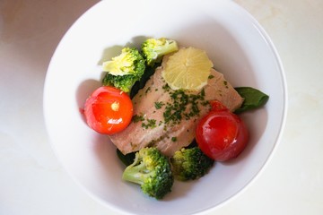 Poached salmon salad in a bowl with brocolli, tomatoes and lemon.