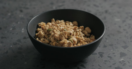 whole grain granola with hazelnuts and pumpkin seeds in black bowl on terrazzo countertop
