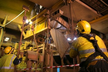 Wide angle picture of rope access riggers wearing safety harness, helmet commencing pulling a heavy...