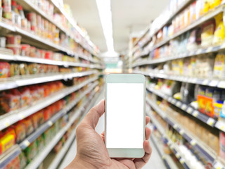 Hand holding smart phone or mobile phone on convenience store shelves interior blur background , Blur Supermarket shelves  