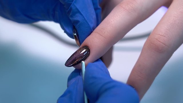 Closeup view of hands of professional manicurist doing modern trendy holiday naildesign using magnets and special glossy sparkling gel polish with shiny cats eye effect. Real time 4k video footage