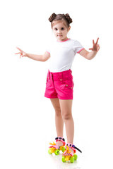 Small positive girl in stylish clothing standing on rollers and smiling over white background