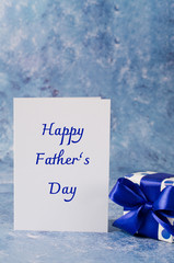 Happy Fathers Day concept. Gift box with ribbon. Heart shaped chalkboard on blue background.