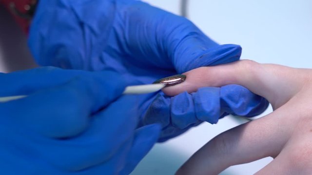 Closeup view of hands of client and professional manicurist doing modern trendy black manicure with magnet cat eye effect. Master of naildesign using special orange stick to remove unwanted gelpolish.