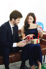 Sweet couple Love smile and spending Romantic christmas time and celebrating new year eve, birthday, and valentine on Brown Sofa decoration with colorful balloon and Gift Boxes in Living room at home