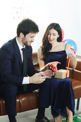 Sweet couple Love smile and spending Romantic christmas time and celebrating new year eve, birthday, and valentine on Brown Sofa decoration with colorful balloon and Gift Boxes in Living room at home