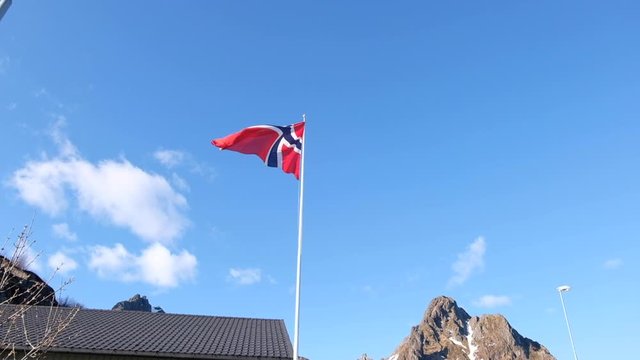 Norwegian Flag waving in the wind in slow motion at the Lofoten Islands. Mountain Peak in Background.