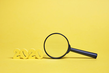 Wooden figures 2020 near magnifier glass on a yellow background.