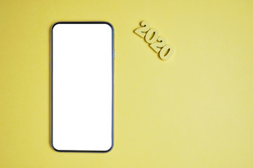 Abstract year 2020 of wooden letters next to a smartphone on a yellow background. Top view. Mock up. Copy space.
